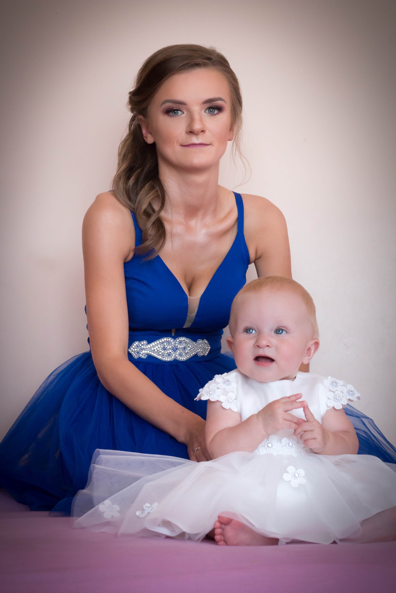 Portret matki w kobaltowej sukni i dziecka w białej sukience z kwiatkami, siedzących na fioletowym tle.