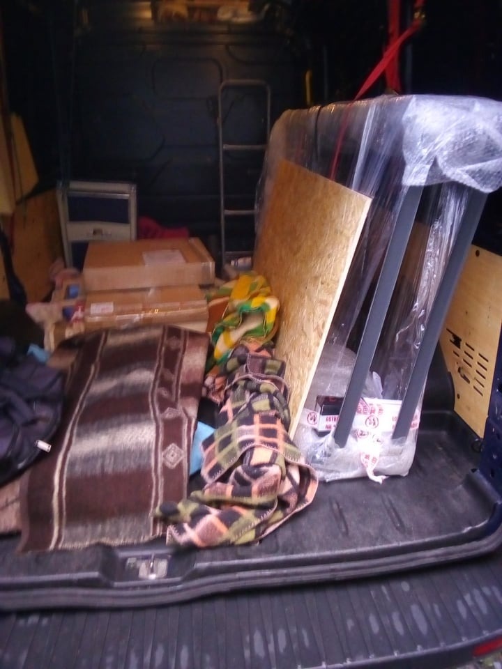 Wnętrze bagażnika busa załadowane kartonami, kocami i meblami zabezpieczonymi folią, przygotowanymi do przewozu.