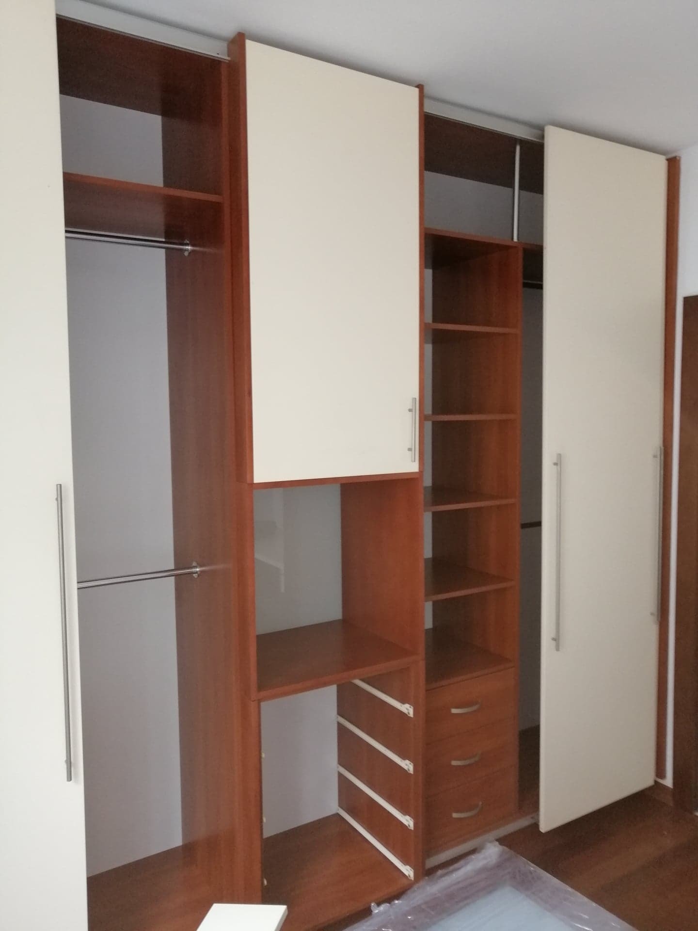 Rozmontowana szafa z brązowymi bokami i kremowymi drzwiami, widoczne półki, szuflady i drążek na ubrania, zdjęcie z wnętrza mieszkania.