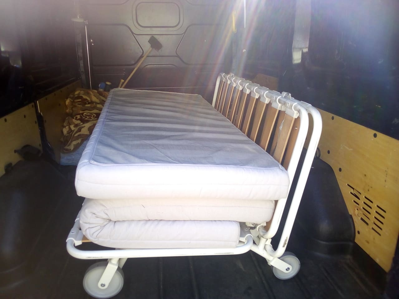 Łóżko szpitalne składane na kółkach, przewożone wewnątrz ciemnego busa transportowego z drewnianą podłogą i ścianami.