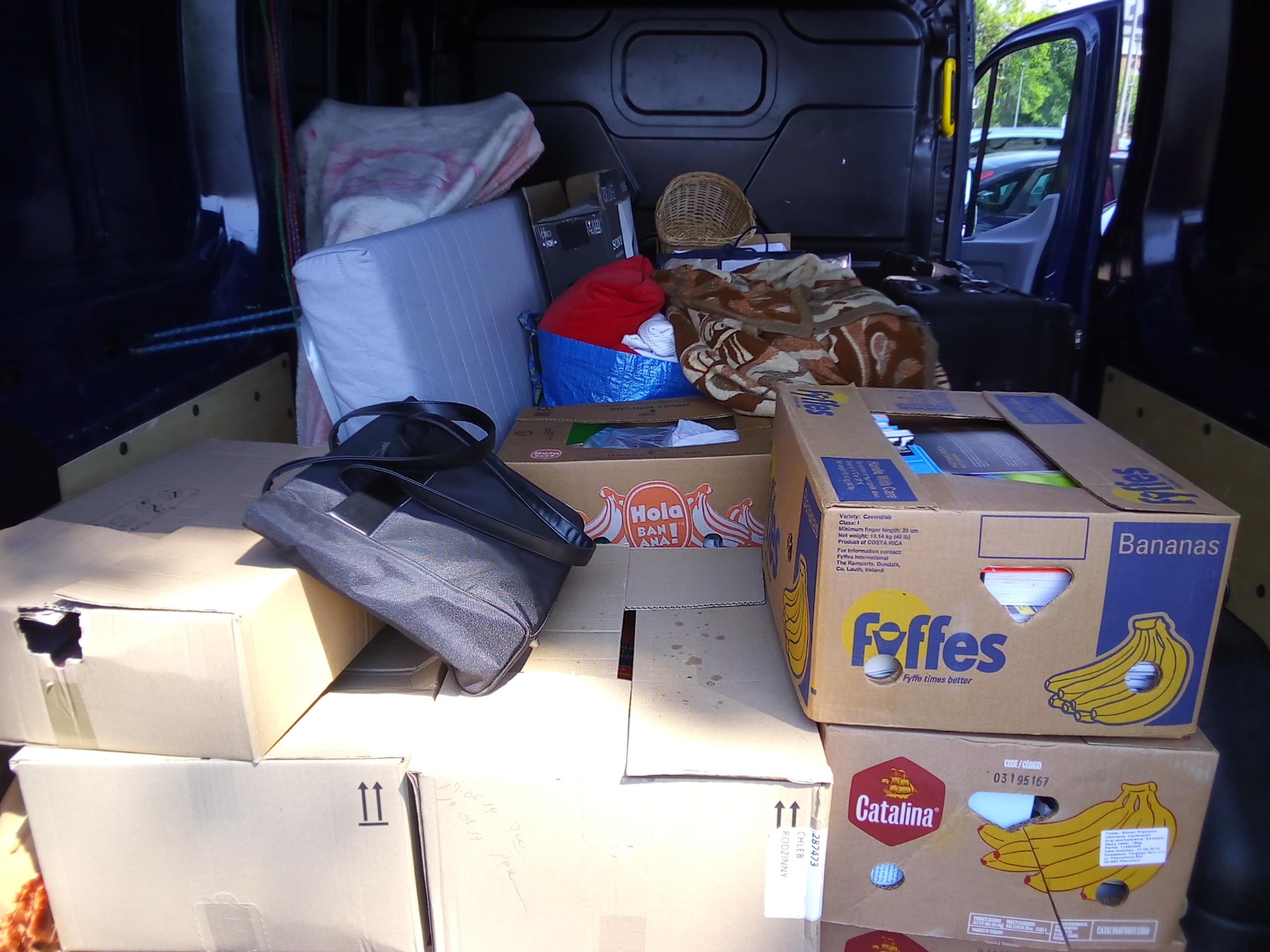 Wnętrze furgonetki załadowane kartonami, torbą i innymi przedmiotami podczas transportu, widoczne otwarte drzwi boczne.