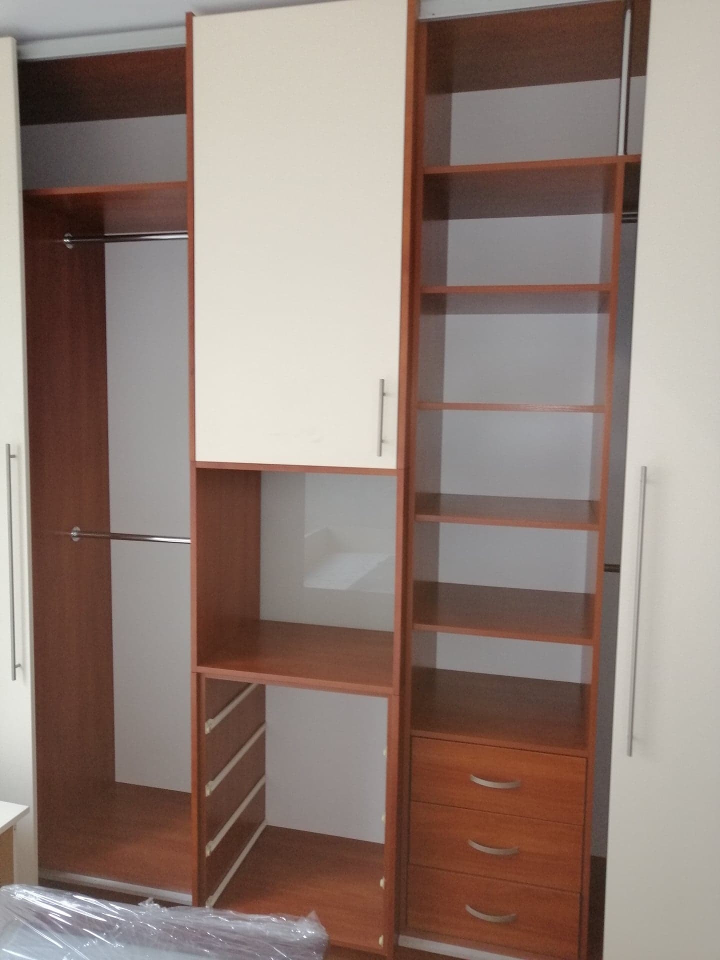 Wnętrze szafy wnękowej z półkami, drążkami i szufladami, wykonanej z drewna w odcieniach brązu i bieli, z widocznym fragmentem podłogi.