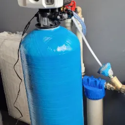 Niebieski zbiornik systemu filtracji wody z elektronicznym sterowaniem, podłączony do instalacji wodnej, widoczny filtr wstępny.