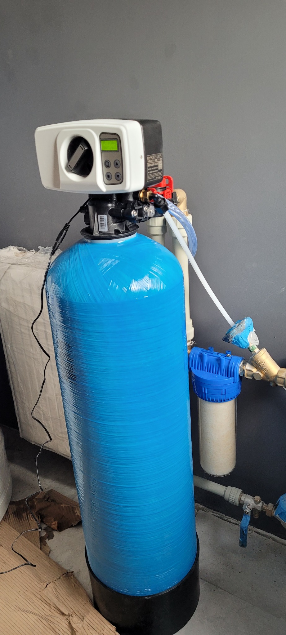 Niebieski zbiornik systemu filtracji wody z elektronicznym sterowaniem, podłączony do instalacji wodnej, widoczny filtr wstępny.