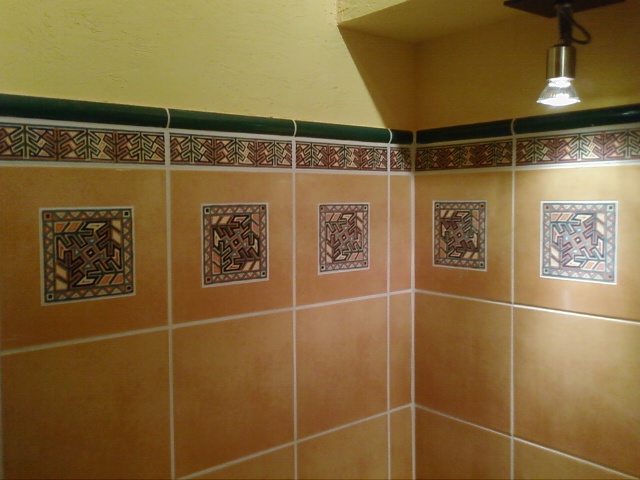 Fragment wykończonej łazienki z brązowymi płytkami z geometrycznym wzorem, zielonym paskiem dekoracyjnym i oświetleniem halogenowym.