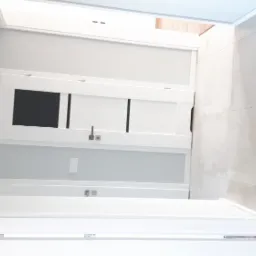 Nowoczesna łazienka w odcieniach bieli i szarości, z minimalistycznymi lampami ściennymi, dużymi płytkami imitującymi beton i białą szafką z frontami w czarne prostokąty.