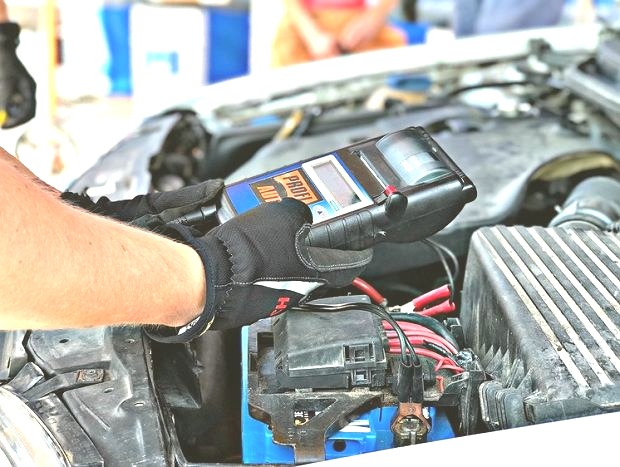 Diagnostyka akumulatora samochodowego w Warszawie przy użyciu profesjonalnego testera; widoczne czarne rękawice robocze i przewody połączeniowe.