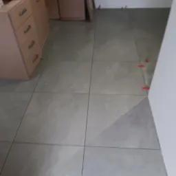 Ułożone szare płytki podłogowe w trakcie prac wykończeniowych w Łagowie, z widocznymi krzyżykami dystansowymi i fragmentem zabudowy kuchennej.