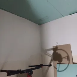 Montaż sufitu z zielonej płyty kartonowo-gipsowej, widoczny podnośnik do płyt i ślady po wkrętach na powierzchni płyty.