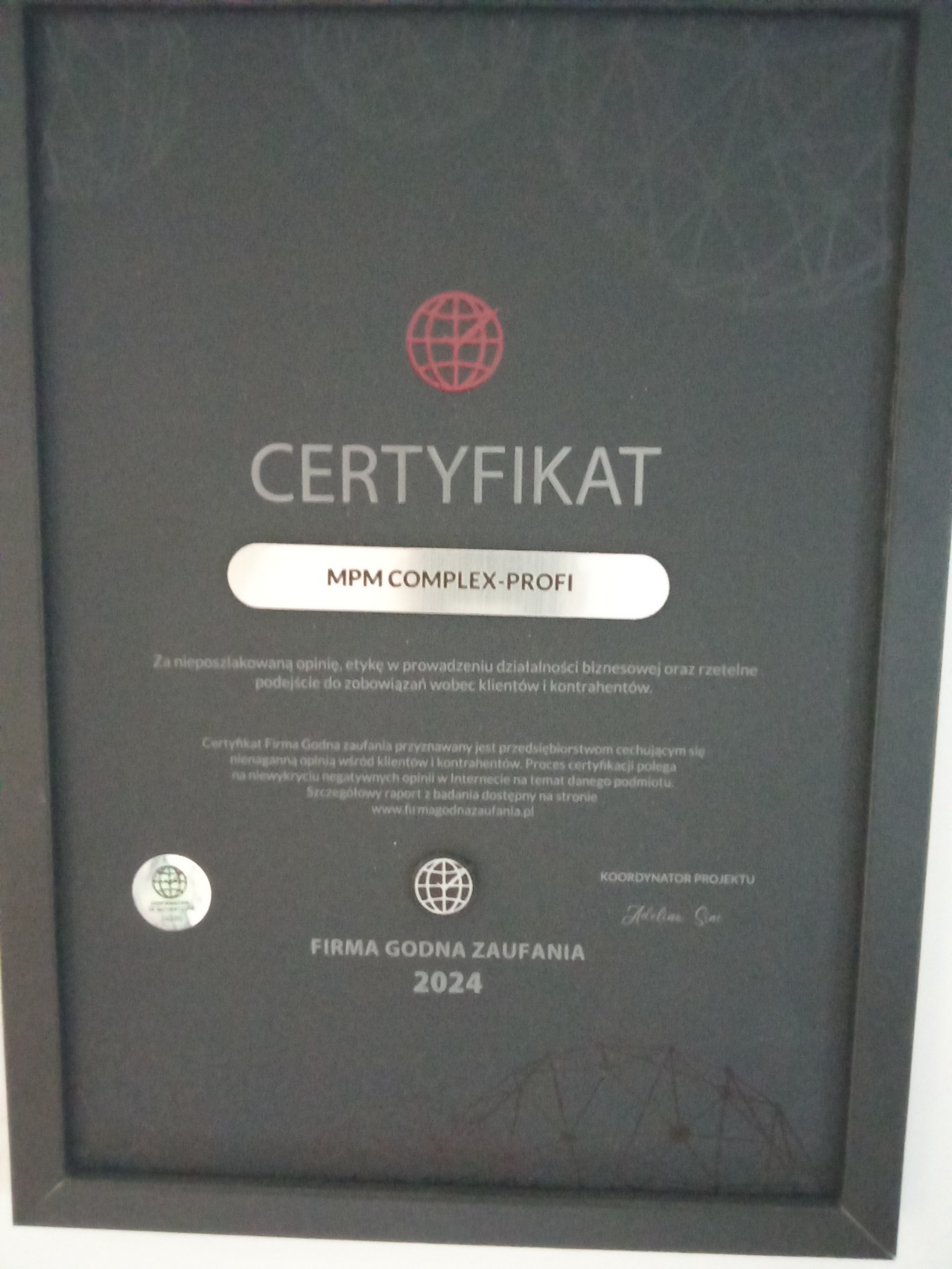 Oprawiony certyfikat 'Firma Godna Zaufania 2024' dla MPM Complex-Profi, potwierdzający rzetelność i etykę w biznesie, z widocznym logo i podpisem koordynatora projektu.