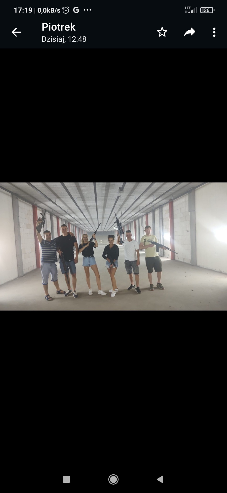 Grupa sześciu osób, w tym dwie kobiety, pozuje z karabinami na strzelnicy; mężczyzna w czarnej koszulce obejmuje kolegę.