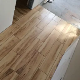 Ułożone pod kątem płytki podłogowe imitujące drewno, widoczne kable wystające ze ściany, surowy stan wykończenia.