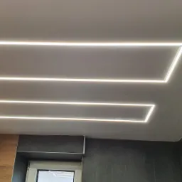 Nowoczesne oświetlenie sufitowe LED w kształcie geometrycznym, w szarej łazience z drewnianymi akcentami, widok z dołu.