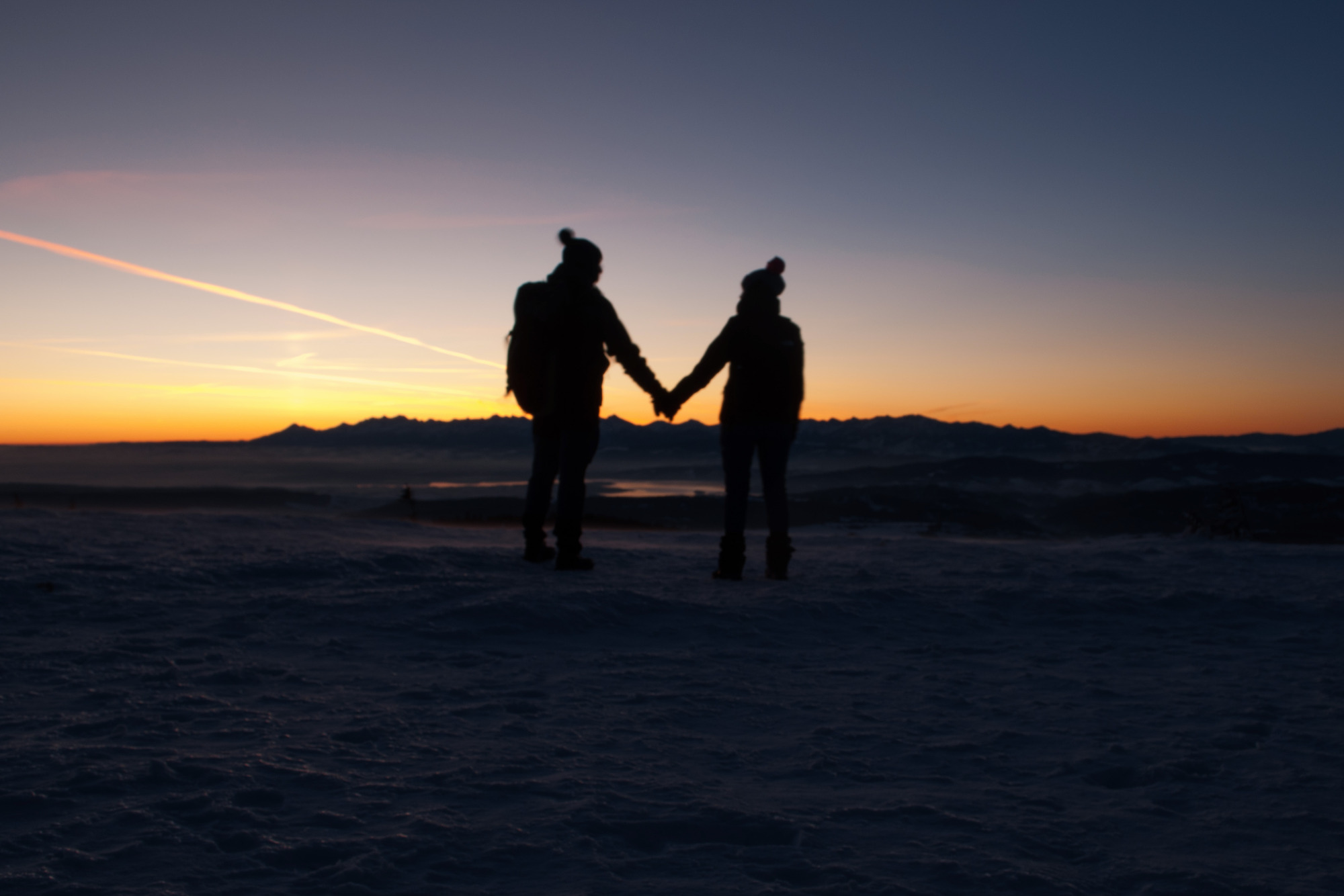 Sylwetki pary trzymającej się za ręce na tle gór o zachodzie słońca, sfotografowane w okolicach Warszawy.