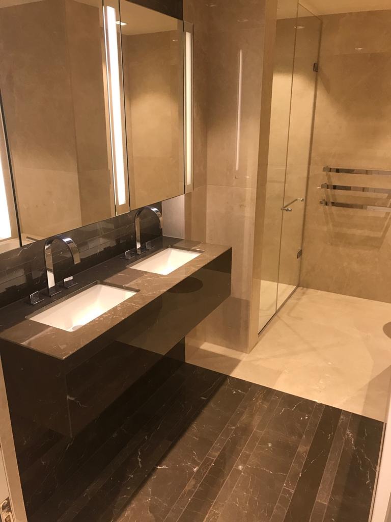 Nowoczesna łazienka z marmurową podłogą w odcieniach brązu, podwójną umywalką na ciemnym blacie i kabiną prysznicową ze szklanymi drzwiami.