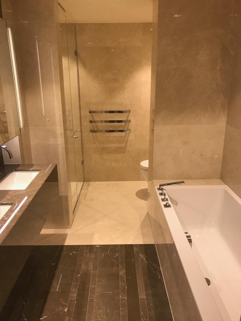 Nowoczesna łazienka z marmurowymi ścianami, kabiną prysznicową ze szklanymi drzwiami, białą wanną i umywalką z blatem z tego samego marmuru, z ciemną podłogą w kontrastującym odcieniu.