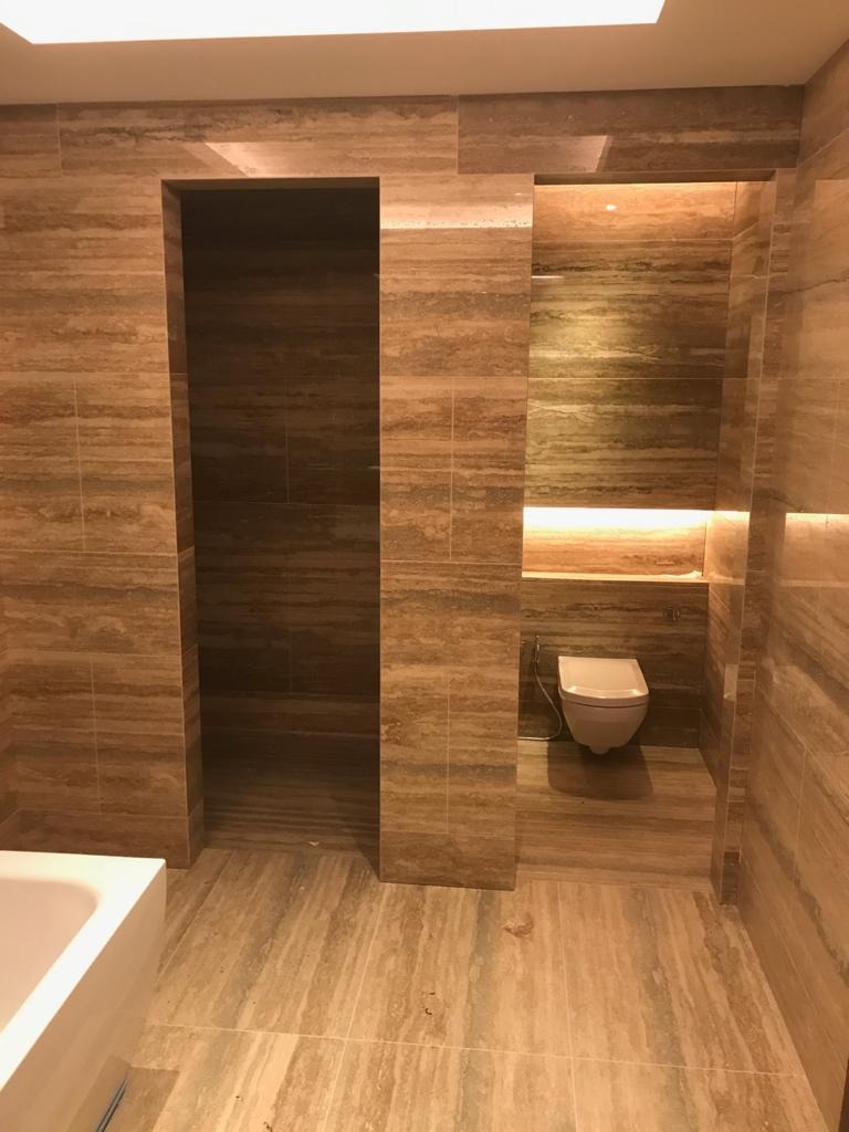 Wykończona łazienka w Jaśle z beżowymi płytkami imitującymi drewno, podświetlona toaleta w niszy i widoczny fragment wanny.