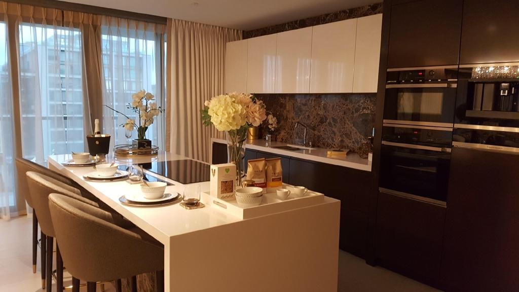 Nowoczesna kuchnia z wyspą, barkiem i krzesłami barowymi, marmurowy panel nad blatem, białe szafki górne i ciemne dolne, zastawa stołowa i dekoracje na blacie, widok na okno z zasłonami.