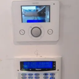 Zestaw domofonowy Opale z panelem alarmowym Texecom zamontowany na białej ścianie, widok z bliska.