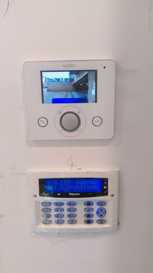 Zestaw domofonowy Opale z panelem alarmowym Texecom zamontowany na białej ścianie, widok z bliska.