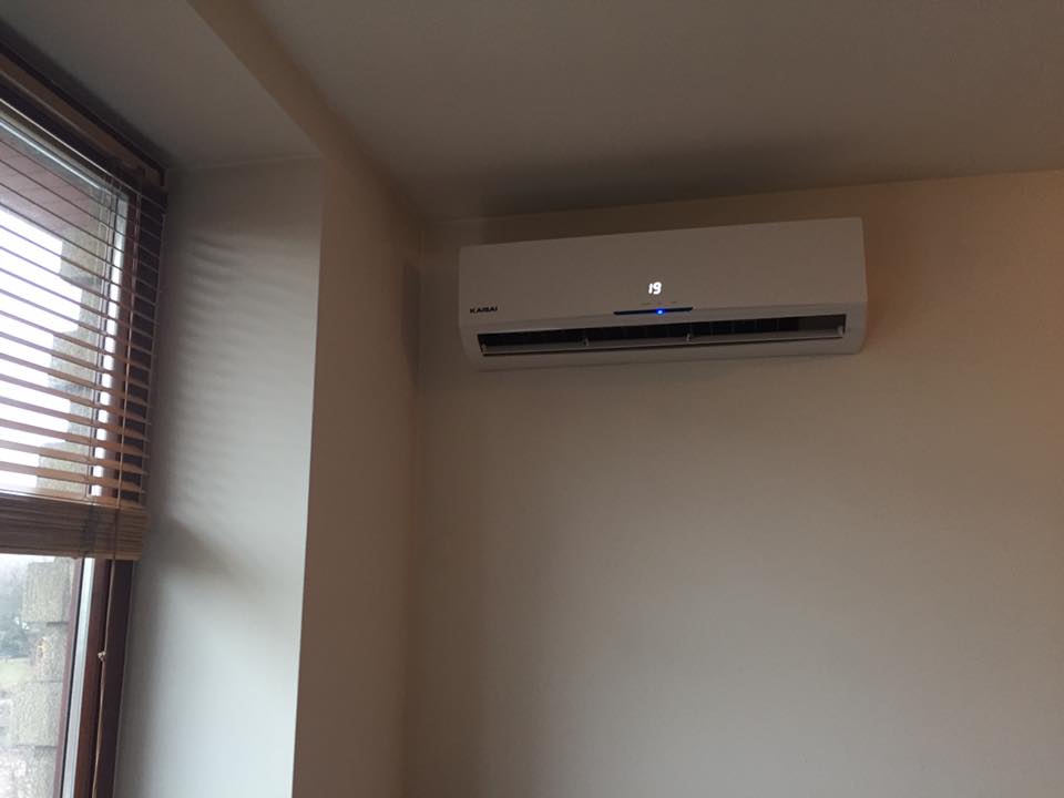 Biały klimatyzator marki Kaisai zamontowany na ścianie w pomieszczeniu z oknem, wyświetlający temperaturę 19 stopni Celsjusza.