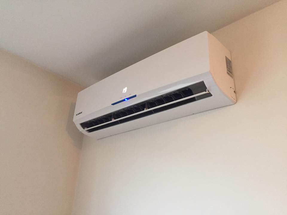 Biały klimatyzator ścienny marki KAISAI z wyświetlaczem temperatury 19 stopni, zamontowany w rogu pokoju o kremowych ścianach.