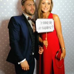 Dobrze.Pstryknięci - Para pozuje ze śmiesznym rekwizytem z napisem 'Ze mną się nie napijesz?' na tle w kropki. Mężczyzna w granatowym garniturze i muszce, kobieta w długiej czerwonej sukni z rozcięciem.