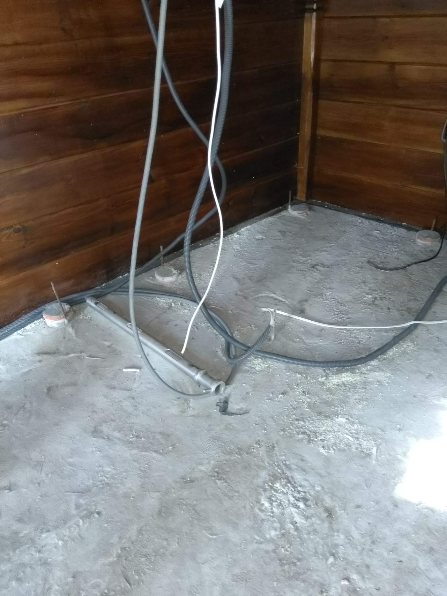 Surowy stan podłogi z wystającymi przewodami i rurami w pomieszczeniu z drewnianą boazerią.