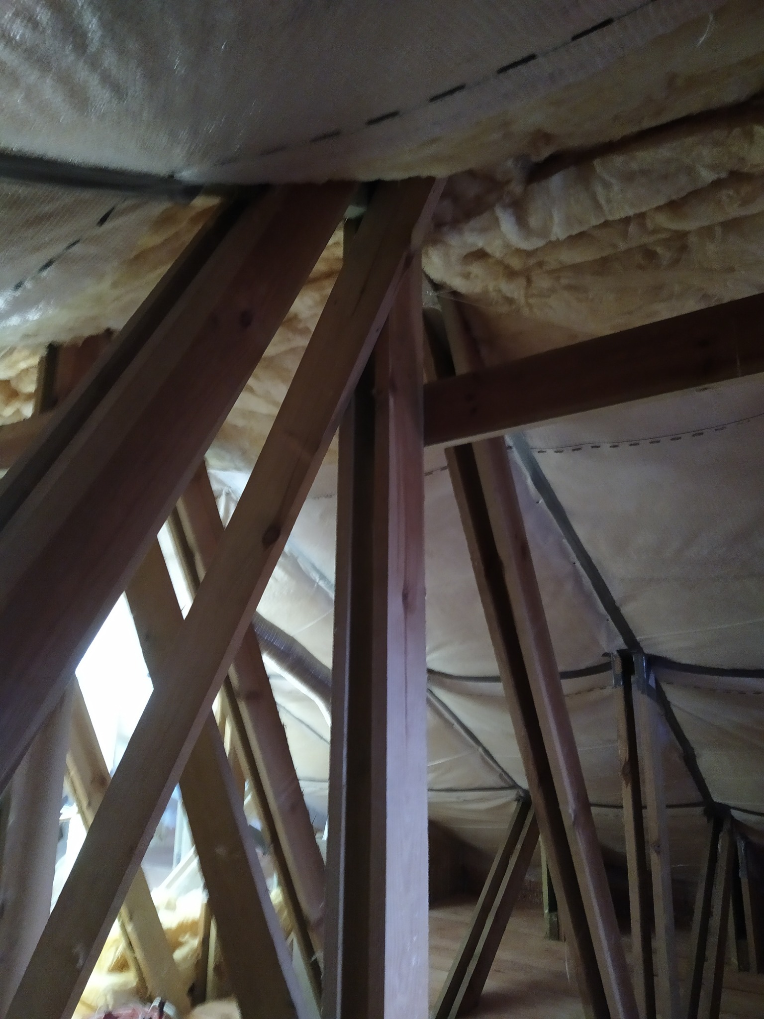 Ocieplenie poddasza wełną mineralną zabezpieczoną folią, widoczne drewniane elementy konstrukcji dachu.