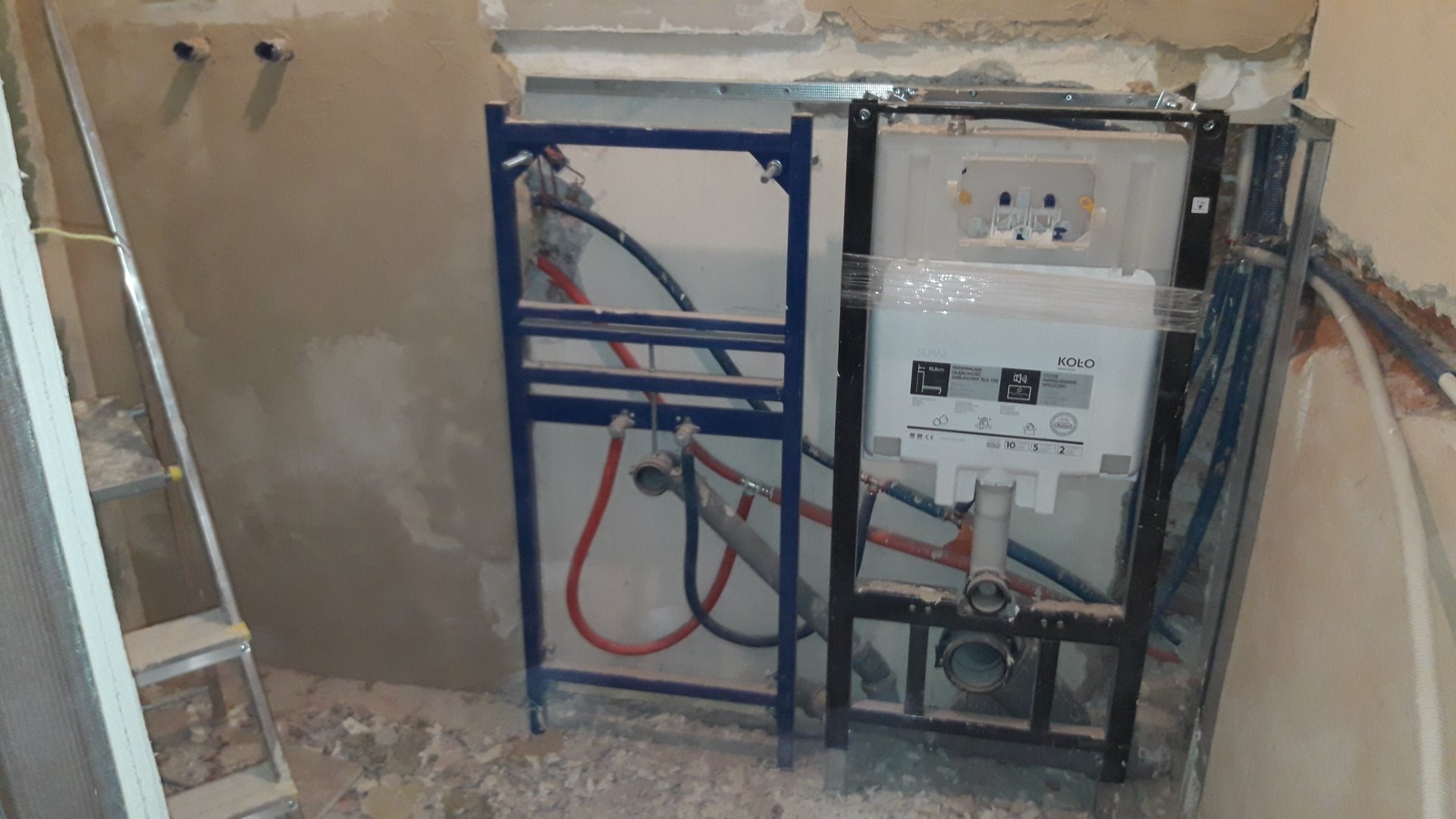 Stelaż podtynkowy WC marki Koło zamontowany w trakcie prac w łazience, widoczne rury doprowadzające wodę i odpływ kanalizacyjny, ściany w stanie surowym.