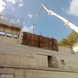 Betonowanie ściany oporowej z deskowaniem systemowym, widoczna pompa do betonu i pracownicy w kaskach.
