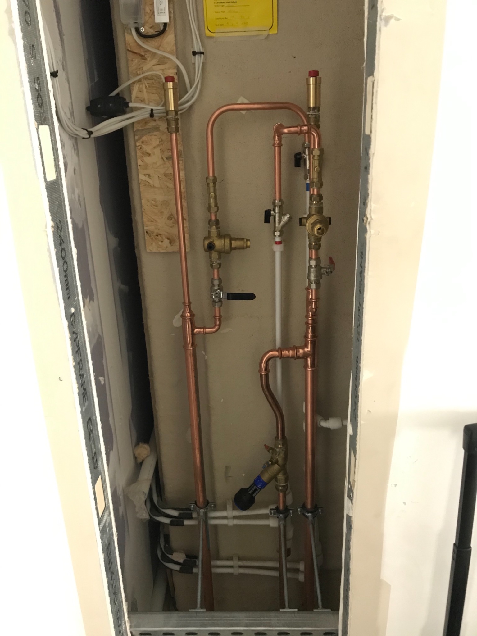 Miedziane rury instalacji hydraulicznej z zaworami, zamontowane w wąskiej wnęce, widoczne przewody elektryczne i elementy mocujące.