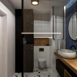 Nowoczesna łazienka z ciemnoniebieską ścianą z płytek ułożonych w jodełkę, okrągłym lustrem z wiszącymi lampami, drewnianym blatem z owalną umywalką i dekoracyjną rośliną w wazonie. Widoczna...