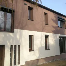 Dwukolorowa elewacja domu jednorodzinnego z brązowymi oknami i drzwiami, z widocznymi elementami dekoracyjnymi z luksferów.