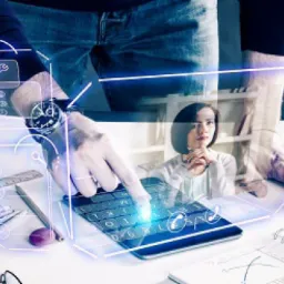 Mężczyzna w koszuli z zegarkiem na ręce, dotyka palcem ekranu tabletu z wyświetlanymi ikonami aplikacji, w tle kobieta siedząca przy biurku, częściowo widoczny regał z dokumentami, całość w tonacji...