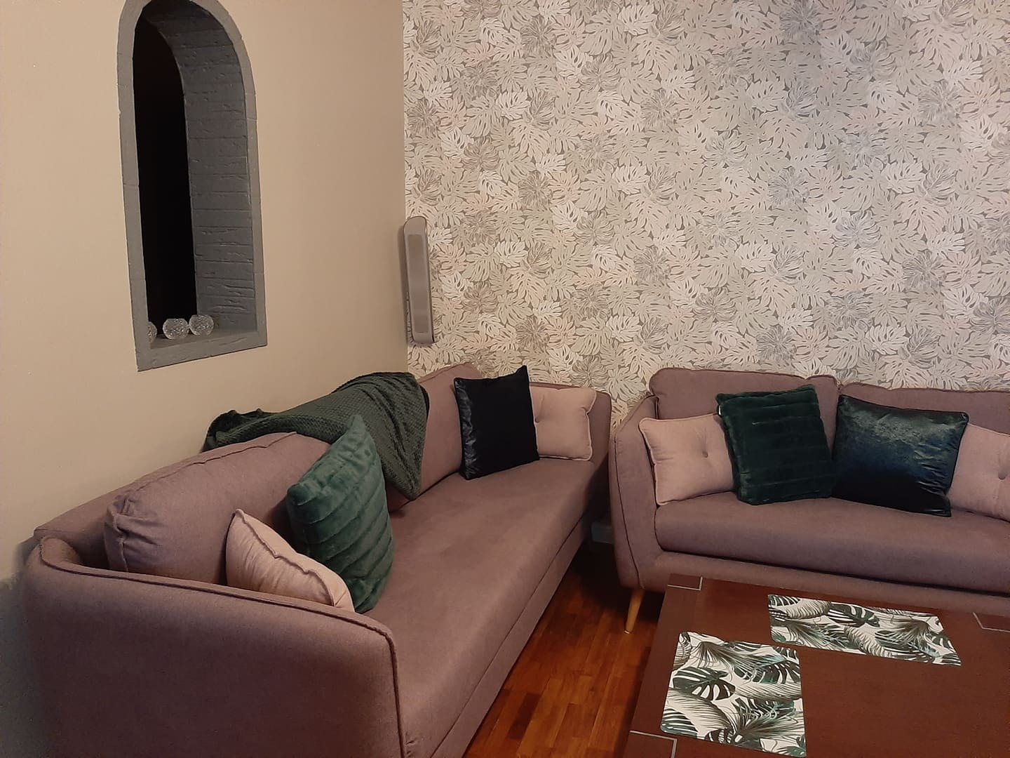 Salon w Katowicach z dwoma sofami w odcieniach fioletu, dekoracyjną ścianą w liście i wnęką w kształcie łuku.