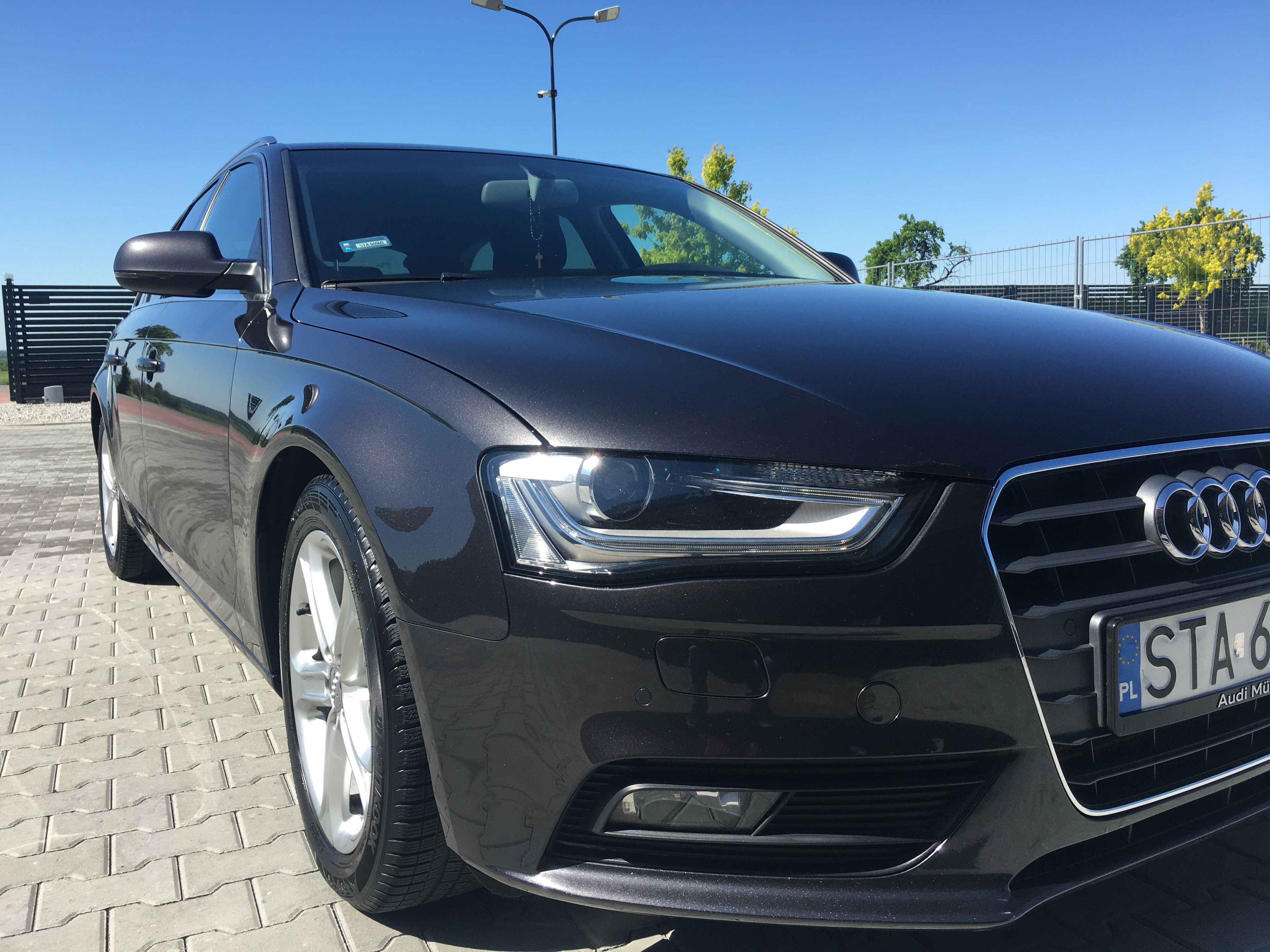 Błyszczący, ciemnoszary samochód osobowy marki Audi po usłudze mycia, zaparkowany na kostce brukowej w Toszku, z widocznym grillem i reflektorem.