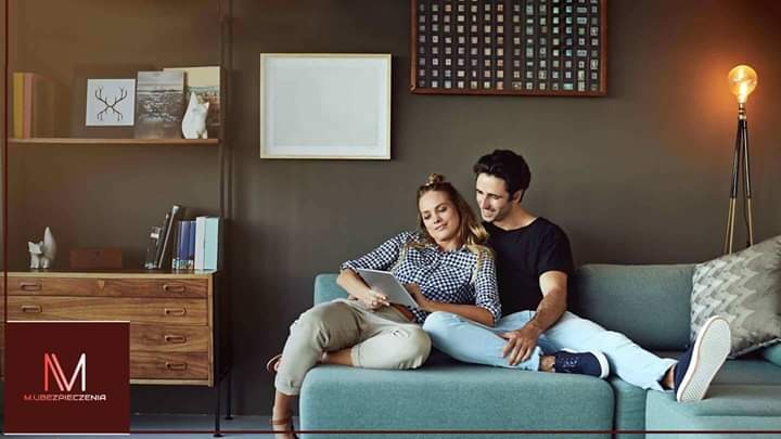 Para relaksuje się na turkusowej kanapie w salonie, kobieta przegląda tablet, w tle komoda z dekoracjami i lampa na trójnogu.