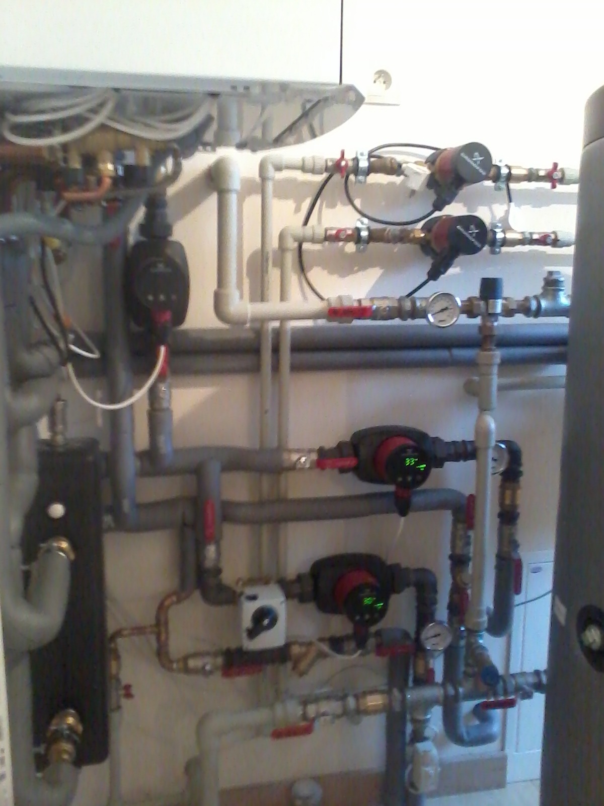 Skomplikowany układ rur, zaworów, pomp obiegowych i manometrów w kotłowni, widoczne elementy instalacji grzewczej i hydraulicznej z bliska.