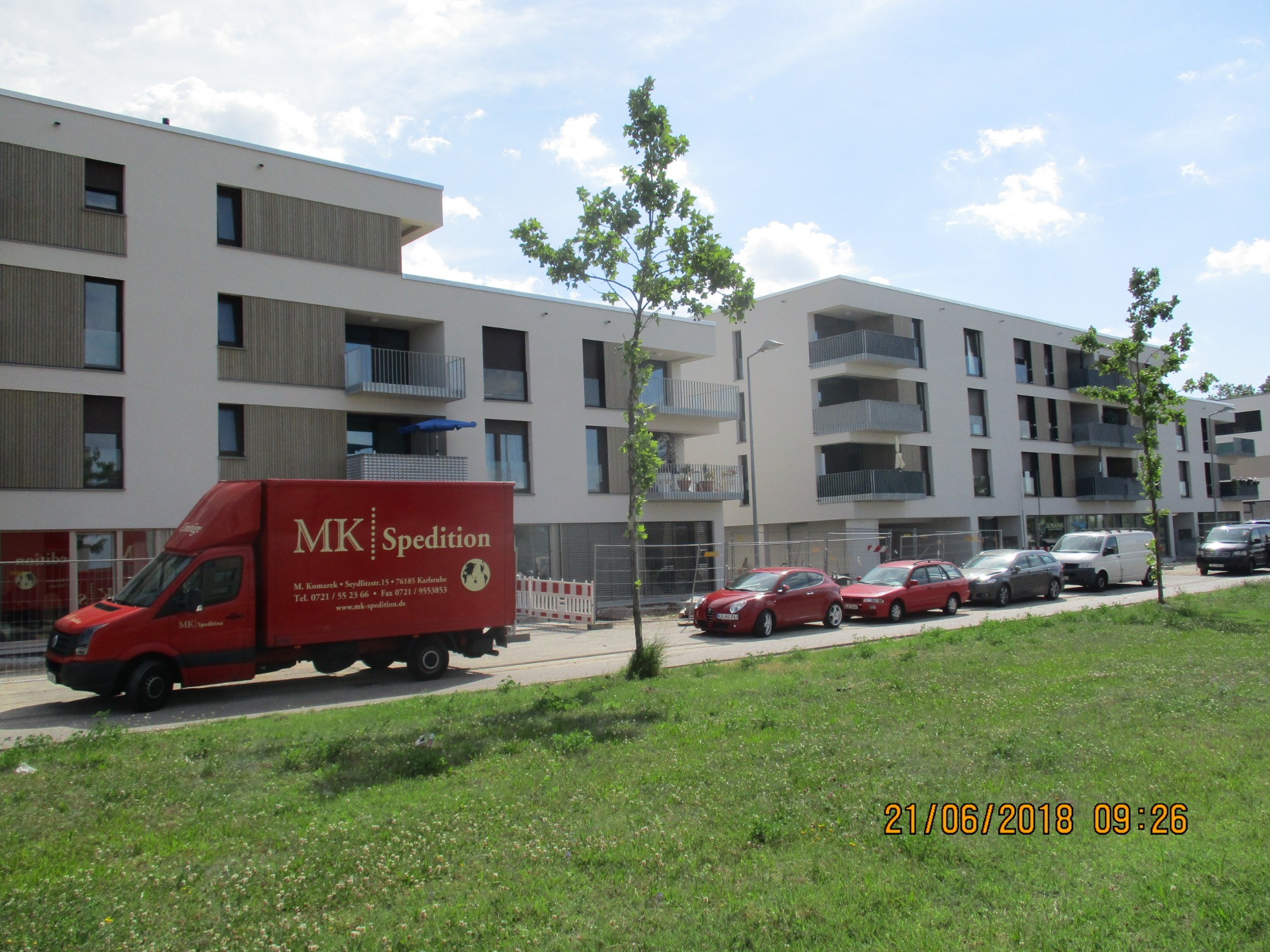 Nowoczesne budynki mieszkalne z balkonami w Karlsruhe, Niemcy, z czerwonym samochodem dostawczym MK Spedition na pierwszym planie.