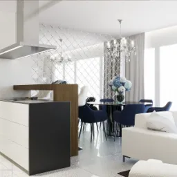Nowoczesne wnętrze: biała kuchnia z czarnym blatem, stół z ciemnymi krzesłami i lustrzana ściana w tle, kryształowy żyrandol nad stołem, biała sofa z poduszką.