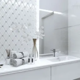 Biała łazienka z umywalką, baterią i dekoracyjnymi płytkami w romby, uzupełniona o zwinięte ręczniki, flakon z kwiatami i akcesoria kosmetyczne.