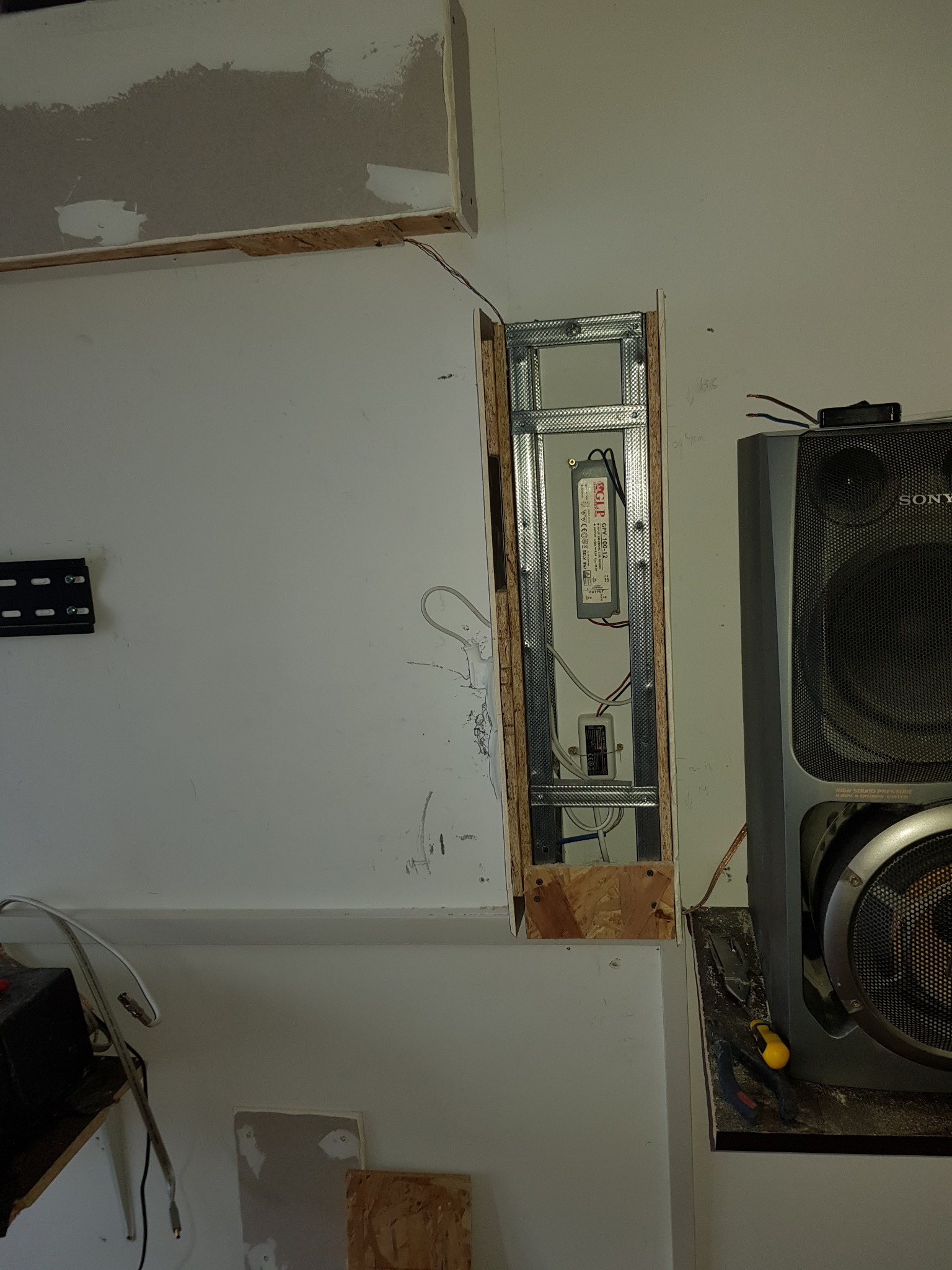 Wnęka w ścianie z widoczną metalową konstrukcją i zamontowanym zasilaczem LED, obok głośnik Sony, widoczne narzędzia.