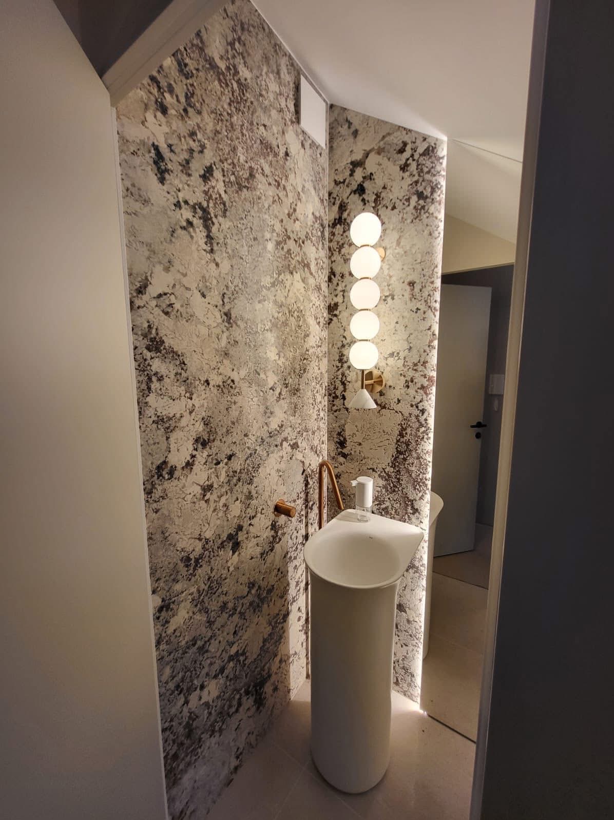 Nowoczesna łazienka z umywalką wolnostojącą, ściany wykończone płytami imitującymi kamień, oświetlenie punktowe. Minimalistyczny design, eleganckie detale.