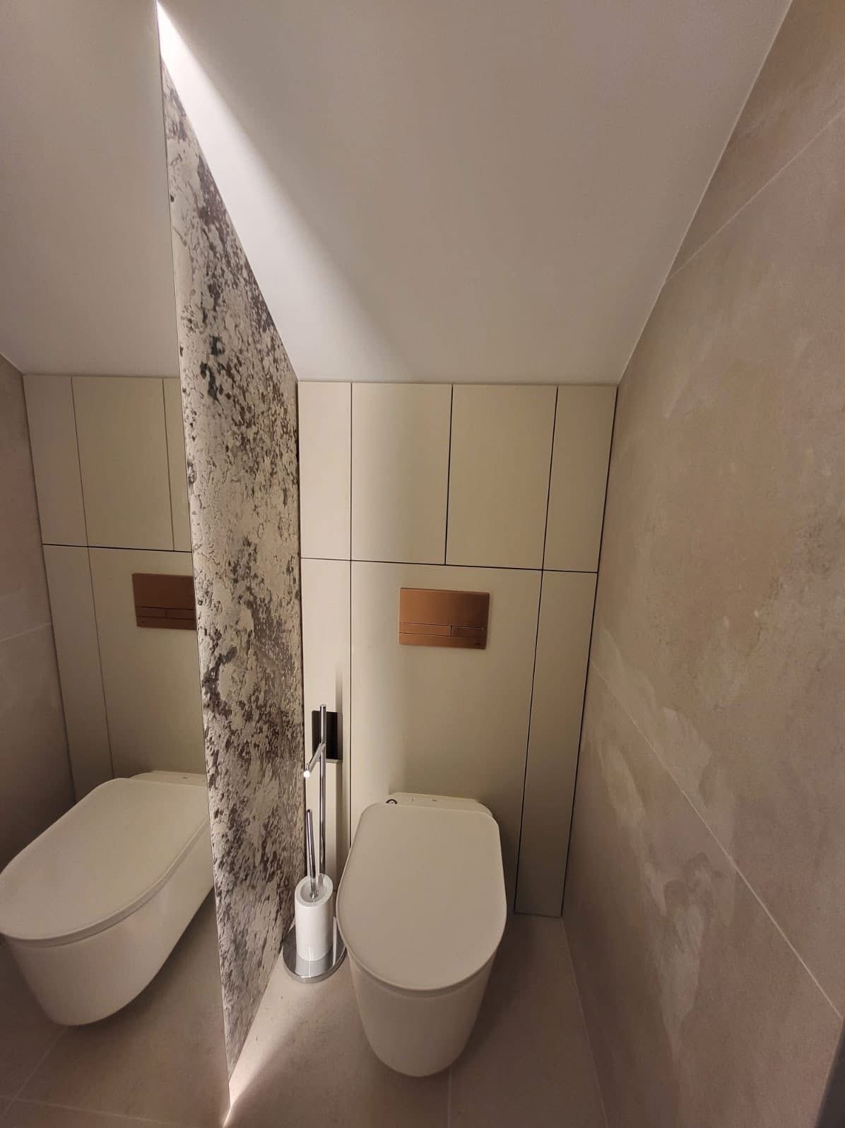 Nowoczesna toaleta z podświetlaną ścianką działową o teksturalnym wzorze, kremowe szafki w zabudowie i beżowe płytki na ścianach. Minimalistyczny design.