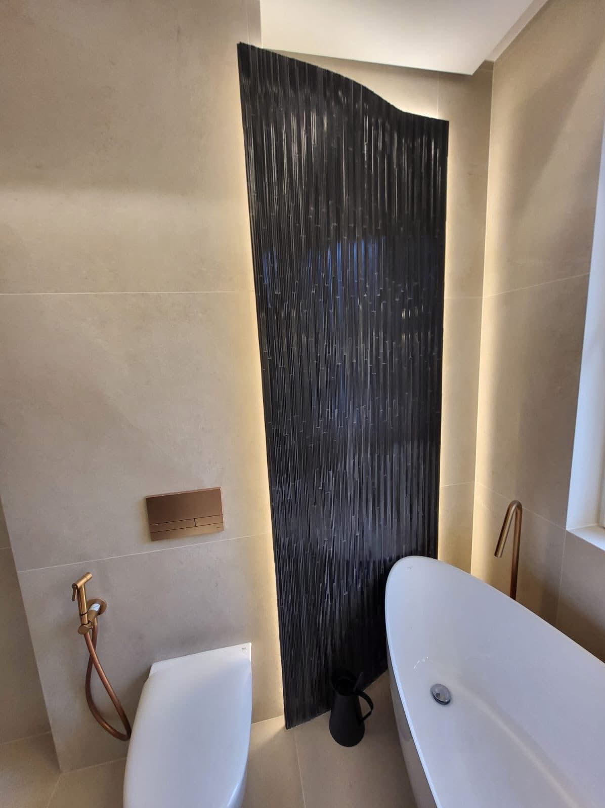 Nowoczesna łazienka z czarną, teksturowaną ścianą podświetloną LED, białą wanną i toaletą. Armatura w kolorze miedzi. Minimalistyczny design.