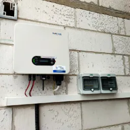 Zamontowany inwerter Sofar Solar na ścianie z betonu komórkowego, widoczne zabezpieczenia w szarych puszkach, okablowanie i puszka instalacyjna powyżej.