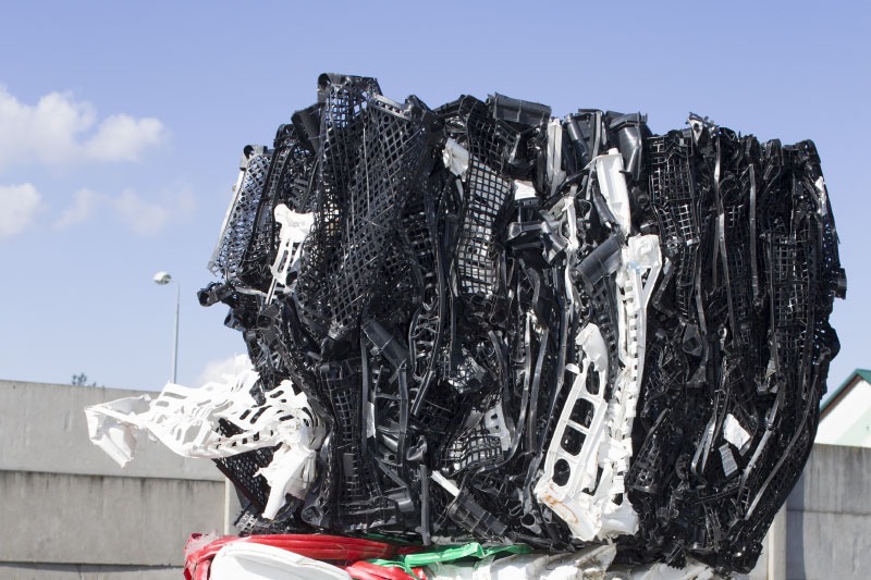 Zbity blok czarnych i białych plastikowych elementów, prawdopodobnie z recyklingu, na tle błękitnego nieba i betonowego muru.