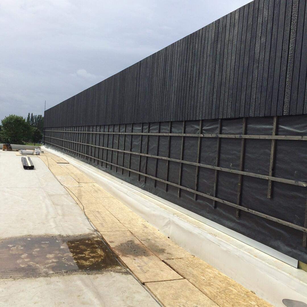 Montaż elewacji z desek opalanych ogniem; widoczne rusztowanie drewniane, membrana wiatroizolacyjna i fragment dachu z papy.