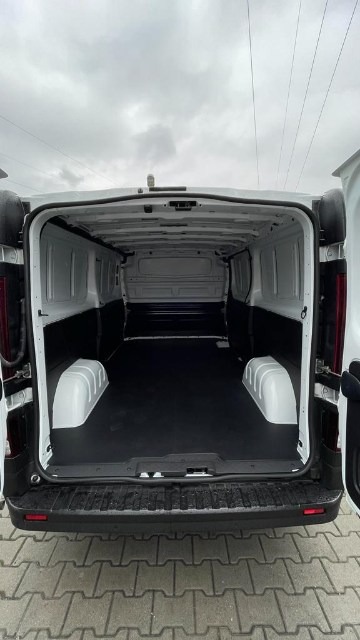 Wnętrze puste, czyste i wyłożone czarną gumą przestrzeni ładunkowej białego samochodu dostawczego z otwartymi drzwiami, widok od tyłu, pochmurne niebo w tle.